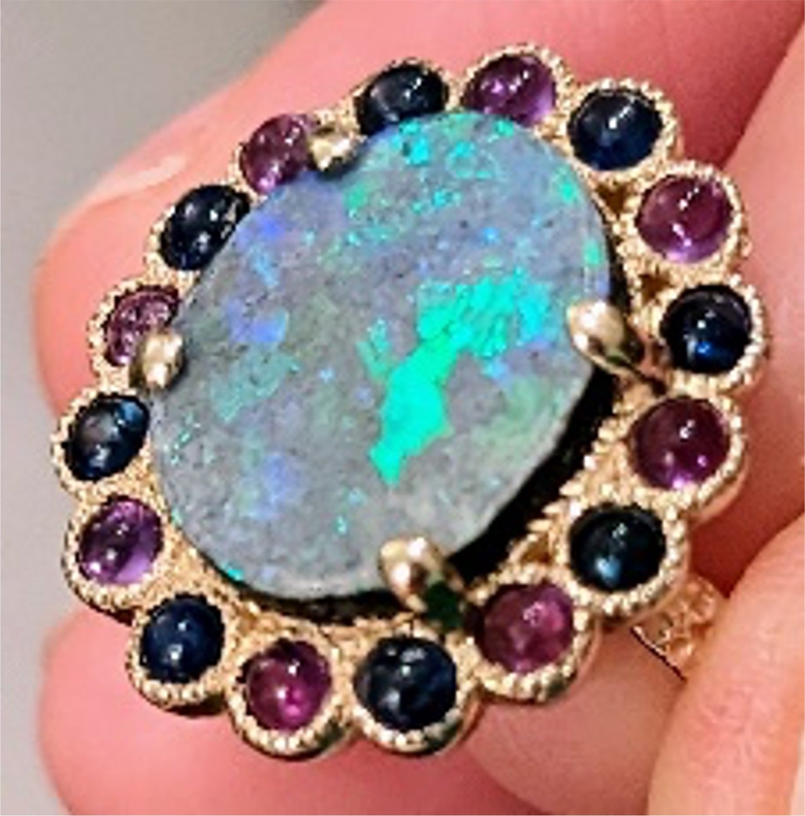 Boulder Opal Ring by Martha Seely available at Talisman Collection Fine Jewelers in El Dorado Hills, CA and online. Stats: Talk about making a statement! This one-of-a-kind ring showcases a 14x12 mm boulder opal surrounded by sapphires and amethyst cabochons. A truly spectacular specimen of nature set in 14k gold. Size 7.2 