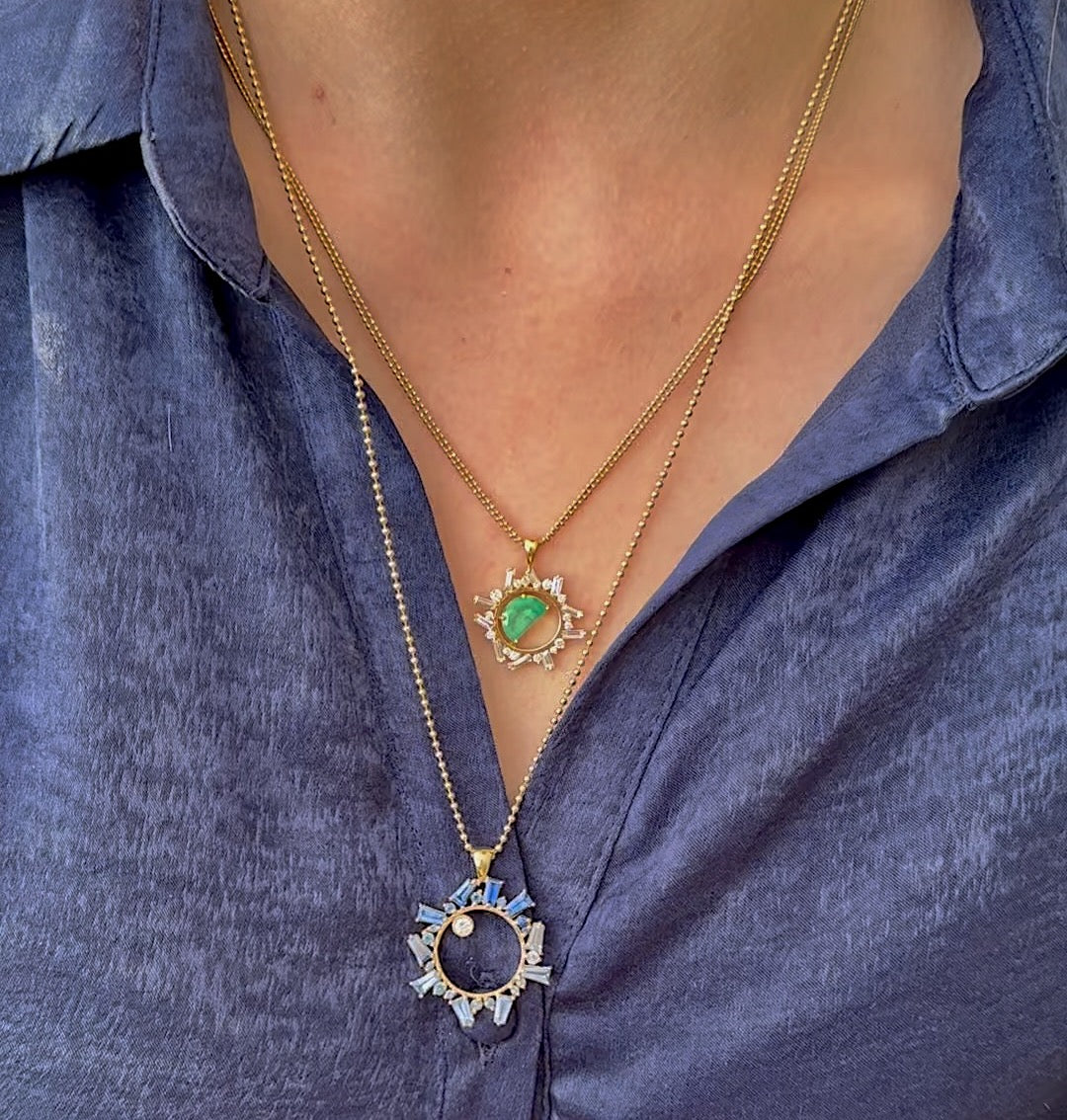 Open Circle Emerald Half Moon Necklace by Meredith Young available at Talisman Collection Fine Jewelers in El Dorado Hills, CA and online. A striking blend of contemporary design and timeless allure, the Controlled Chaos Half Moon Necklace is handcrafted in 18k yellow gold and features a mesmerizing 1.25 ct half-moon Colombian Emerald encased in an open circle frame, surrounded by 1 ctw of white baguette and round diamonds. The unique pendant hangs from a double strand ball chain. 